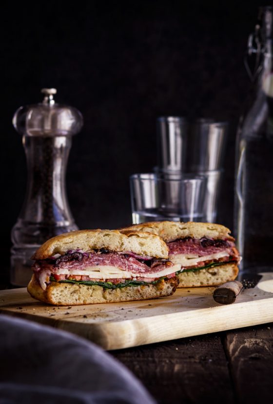 This easy to make muffuletta sandwich recipe is a must for the Italian antipasto lovers. It is made of muffuletta bread infused with fragrant olive oil dressing, layers of gorgeous Italian cold cuts and cheeses. Make this Italian sandwich a day ahead to save some time because this New Orleans pride gets better as it sits. #muffuletta #sandwich #italiansandwich